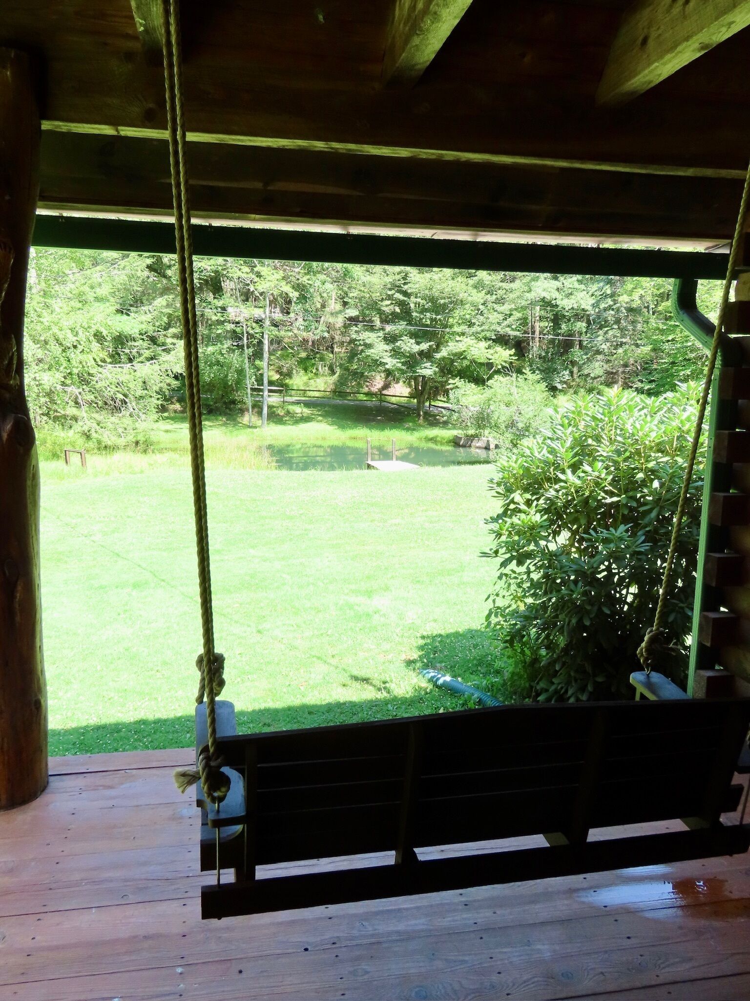 A wooden swing with a view of a grassy yard and trees.