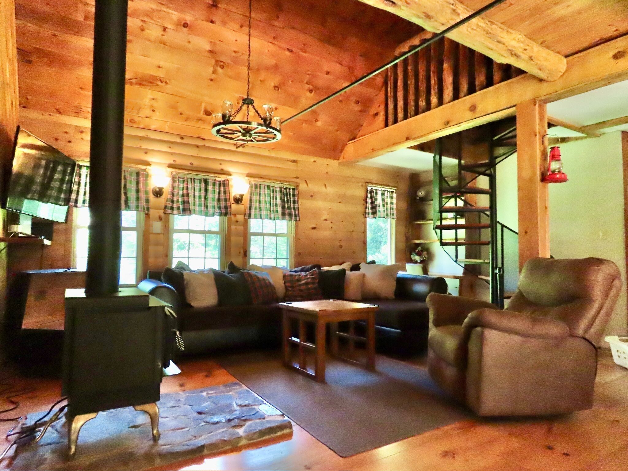 L’intérieur d’un chalet accueillant, avec une cheminée, des murs en bois, un ensemble de canapés et un escalier.