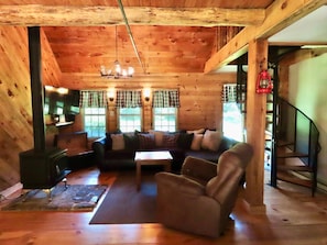 A cozy cabin interior with a wooden ceiling, a sofa, a chair, a table, and a fireplace.