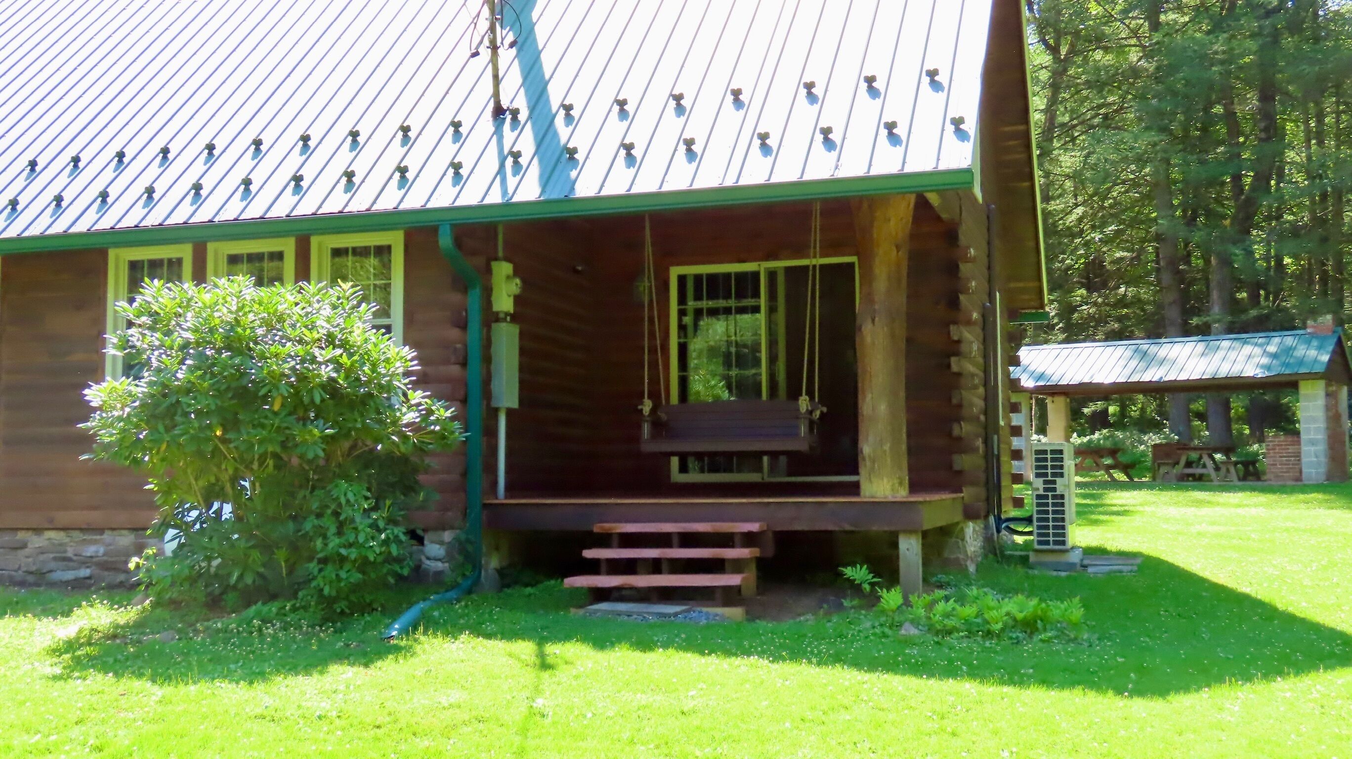 A wooden cabin with a porch, a swing, and a covered picnic area.