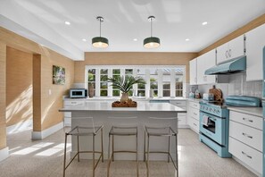 A modern kitchen with a large island, bar stools, a blue stove, and a view of greenery outside. - Pink Palm Retreat - Pineapple Grove (Delray Beach)