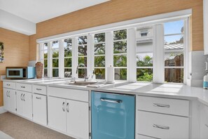 Eine moderne Küche mit weißen Schränken, einem blauen Geschirrspüler und einem großen Fenster mit Blick auf Grünflächen.