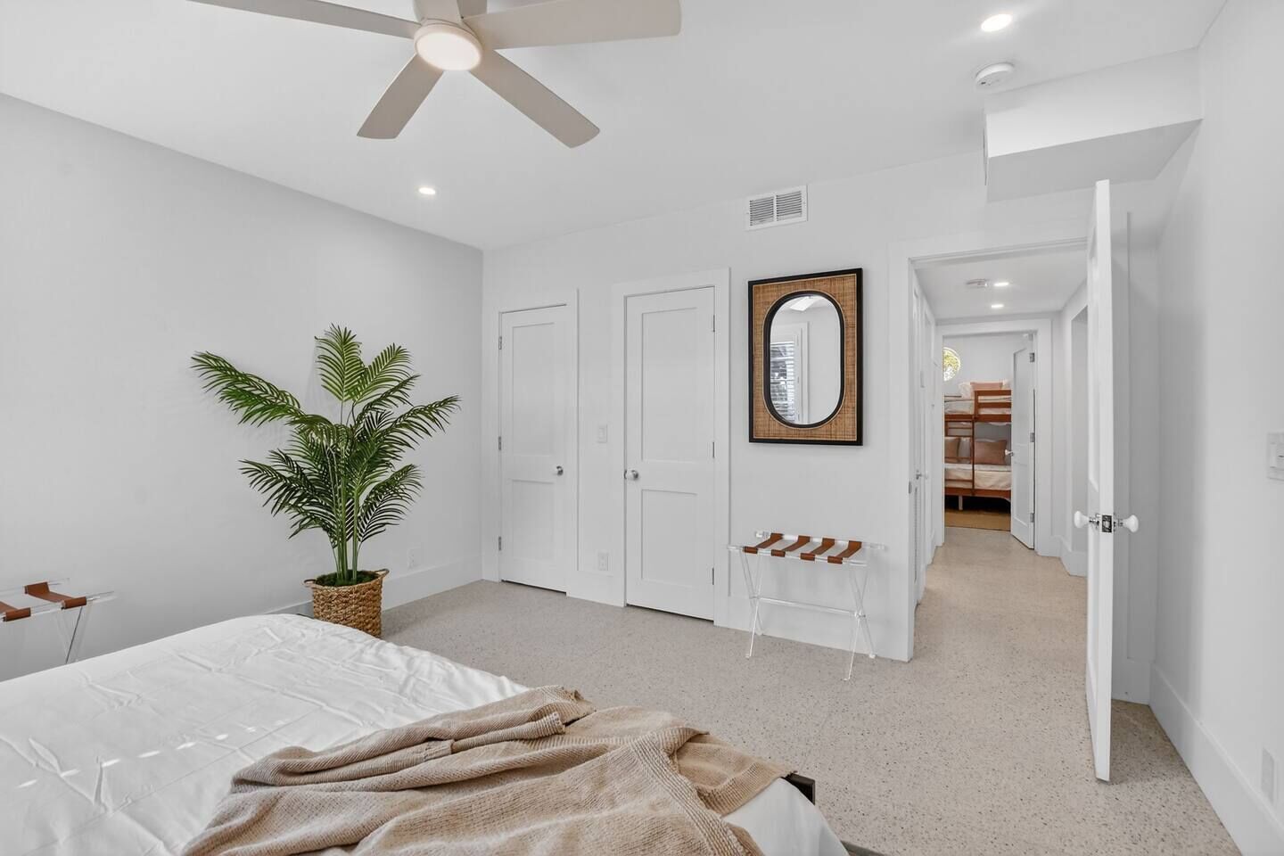 A bedroom with a bed, a ceiling fan, a potted plant, a mirror, and a door leading to another room.