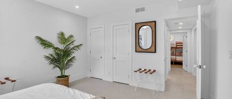 A bedroom with a bed, a ceiling fan, a potted plant, a mirror, and a door leading to another room.