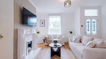 A living room with a fireplace, a television mounted on the wall, a sofa, a coffee table, and a window with blinds.