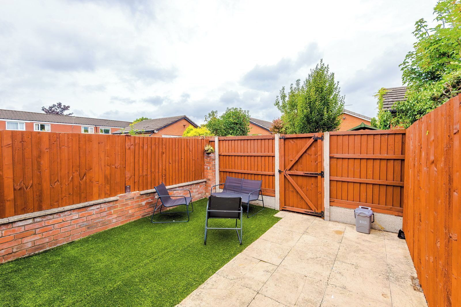 A backyard with a wooden fence, two lawn chairs, a table, and a paved patio area.