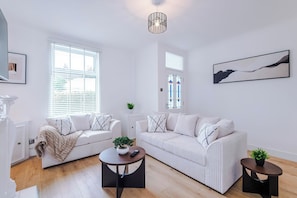 Un salon moderne avec deux canapés blancs, une table basse ronde et une petite table d’appoint sur laquelle est posée une plante.