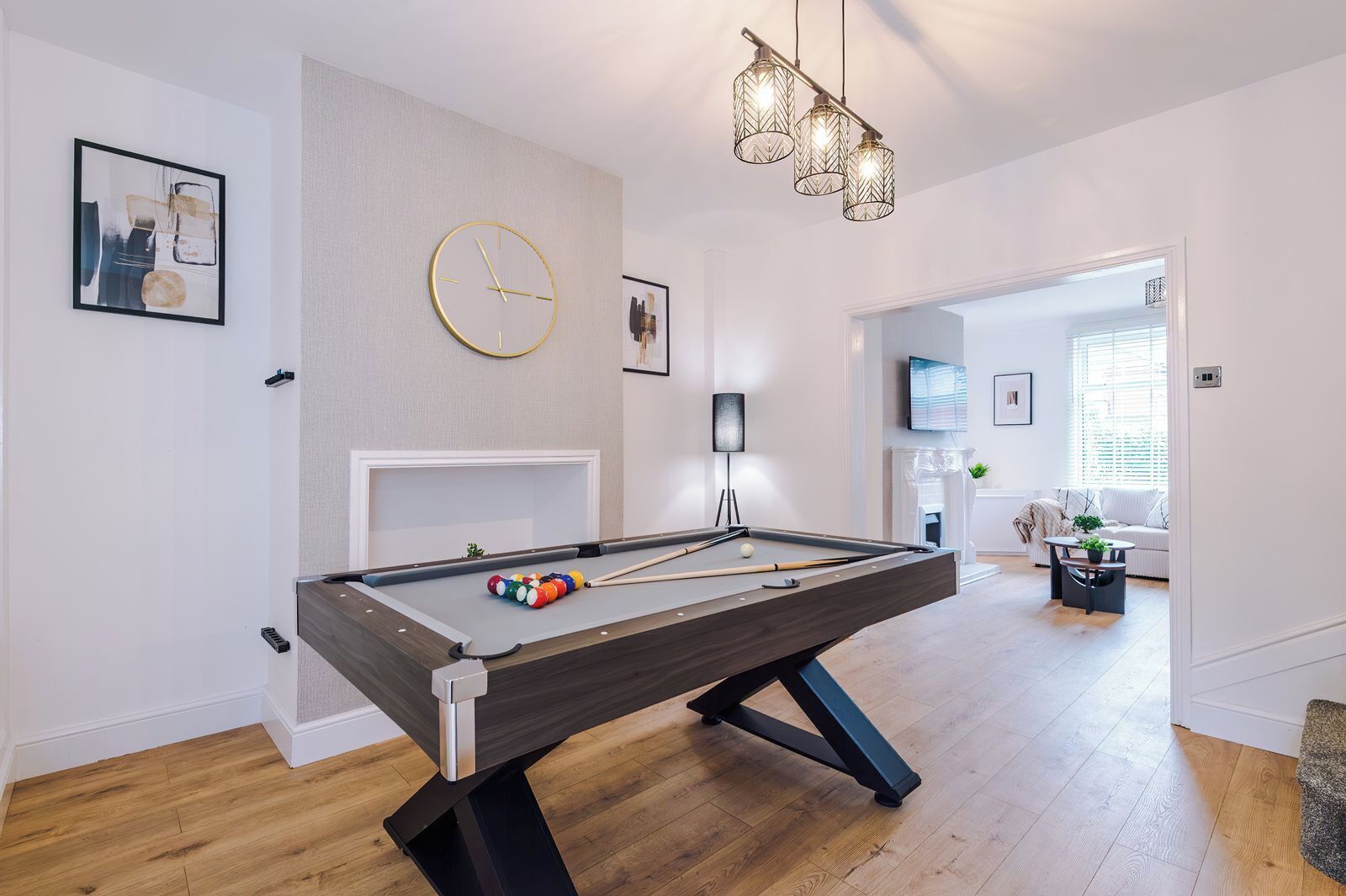 Une table de billard avec une horloge au-dessus, un canapé et un téléviseur dans un espace de vie.