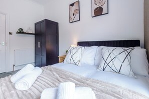Quarto de hotel com cama, guarda-roupa, radiador e duas imagens emolduradas na parede.