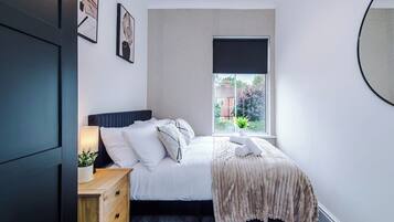 A bedroom with a bed, bedside table, lamp, and a window with a view.