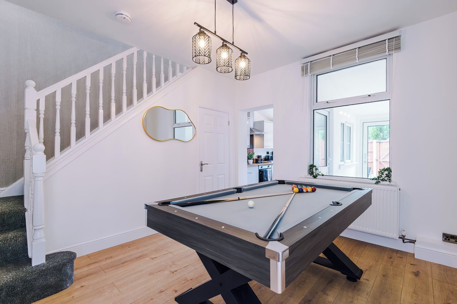 A pool table in a room with a staircase, a large window, and a hanging light fixture.