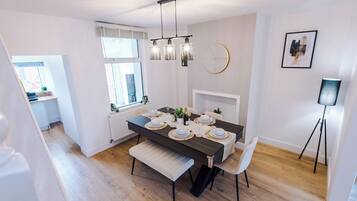 Un coin repas avec une table en bois foncé dressée pour quatre personnes, des chaises blanches, un banc et un lustre moderne.