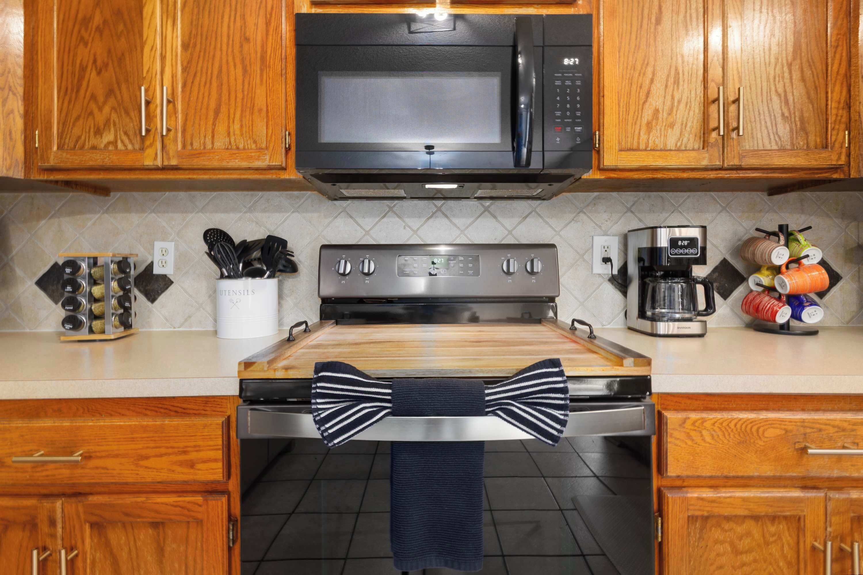 A kitchen with wooden cabinets, a microwave, a stove, a coffee maker, and a spice rack.