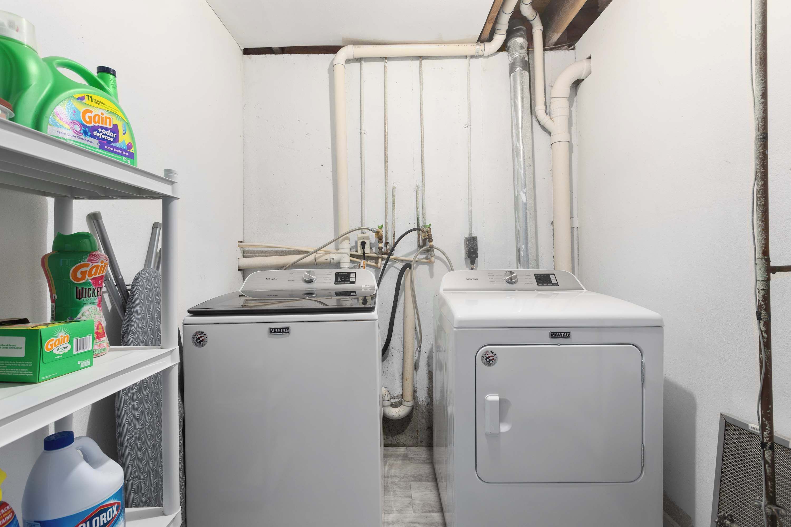 Une buanderie équipée de deux machines à laver Maytag, d’un sèche-linge et de divers produits de nettoyage rangés sur des étagères.