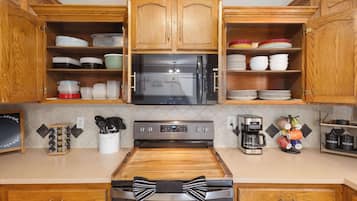Una cocina con armarios de madera, un refrigerador de acero inoxidable, un microondas, una cafetera y diversos utensilios de cocina.