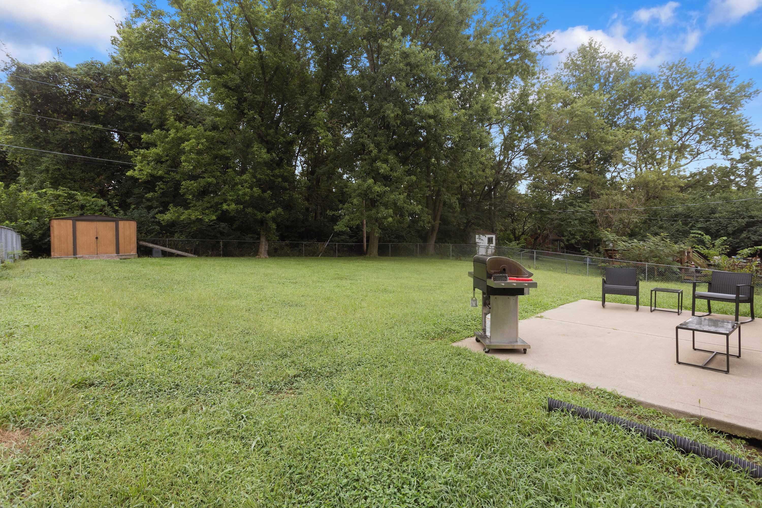 A grassy backyard with a barbecue grill, a small shed, and outdoor furniture.