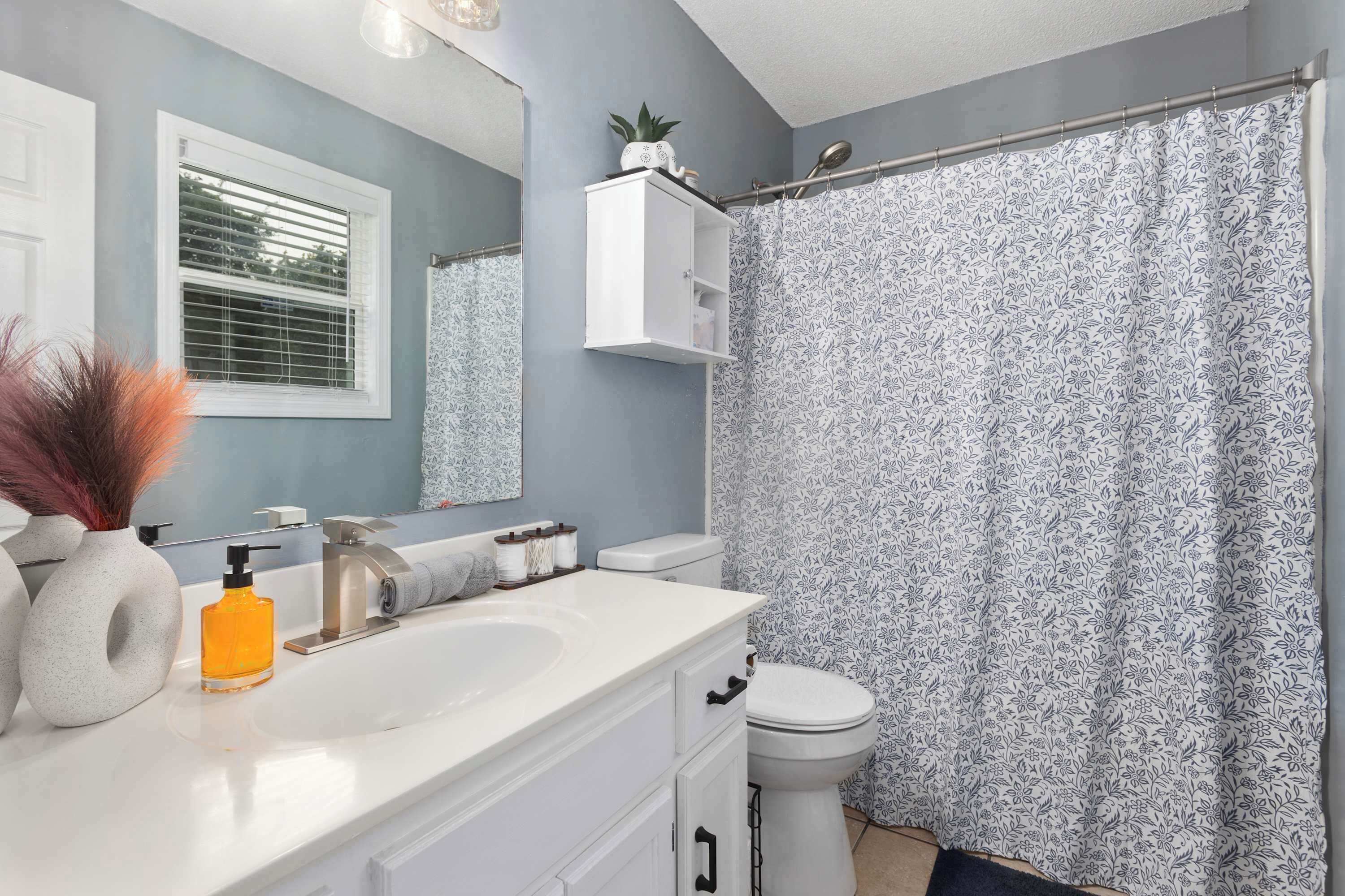Un baño con tocador blanco, espejo, inodoro y cortina de ducha con estampado floral.