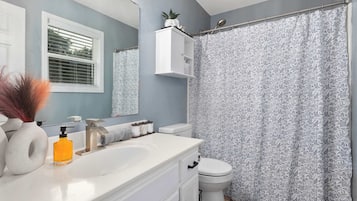 Un baño con tocador blanco, espejo, inodoro y cortina de ducha con estampado floral.