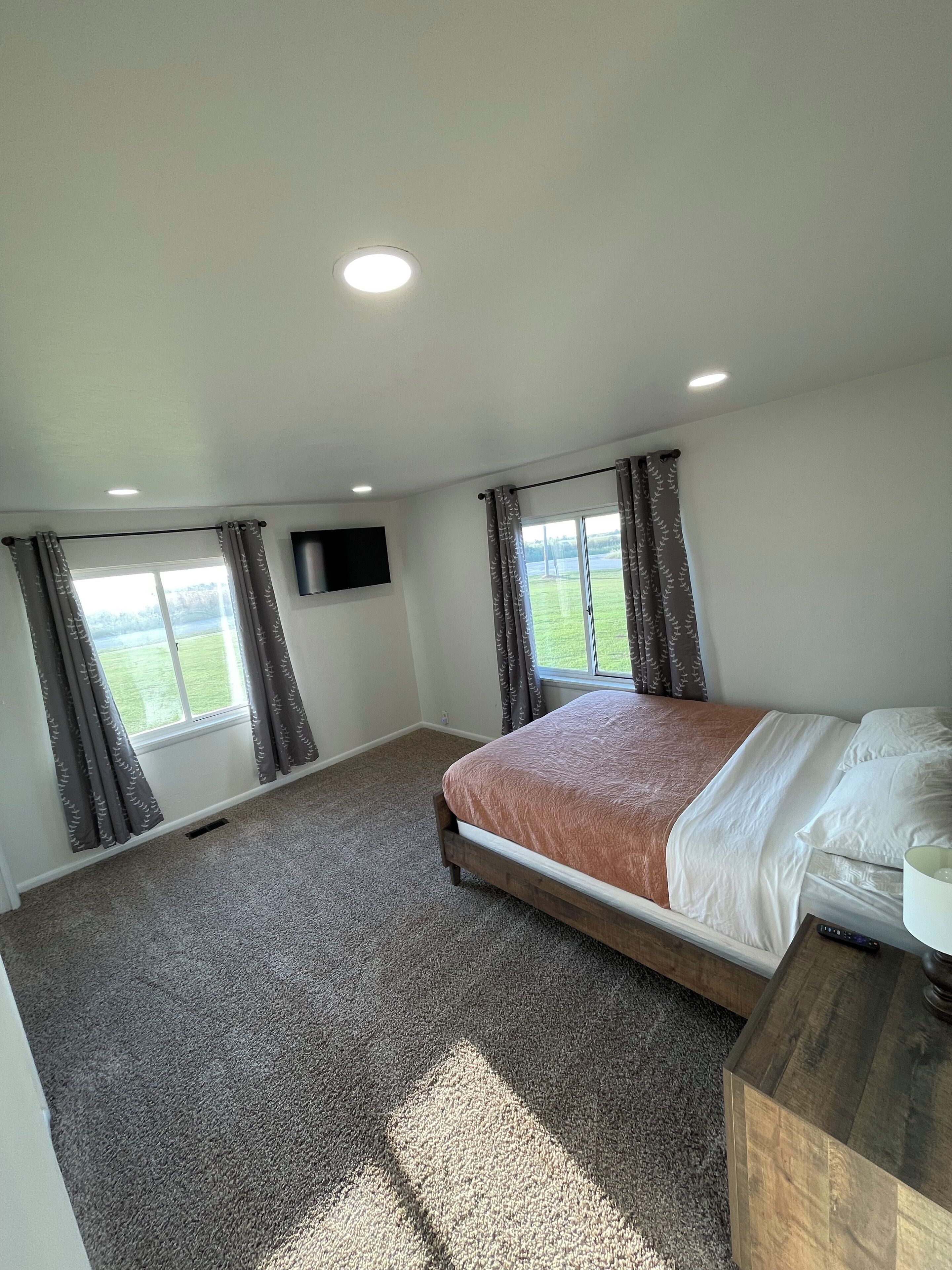 A bedroom with a bed, a TV mounted on the wall, and a window with curtains.