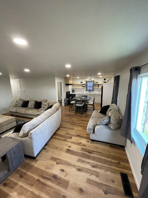 A modern living room with two sofas, a dining table, and a kitchen in the background.