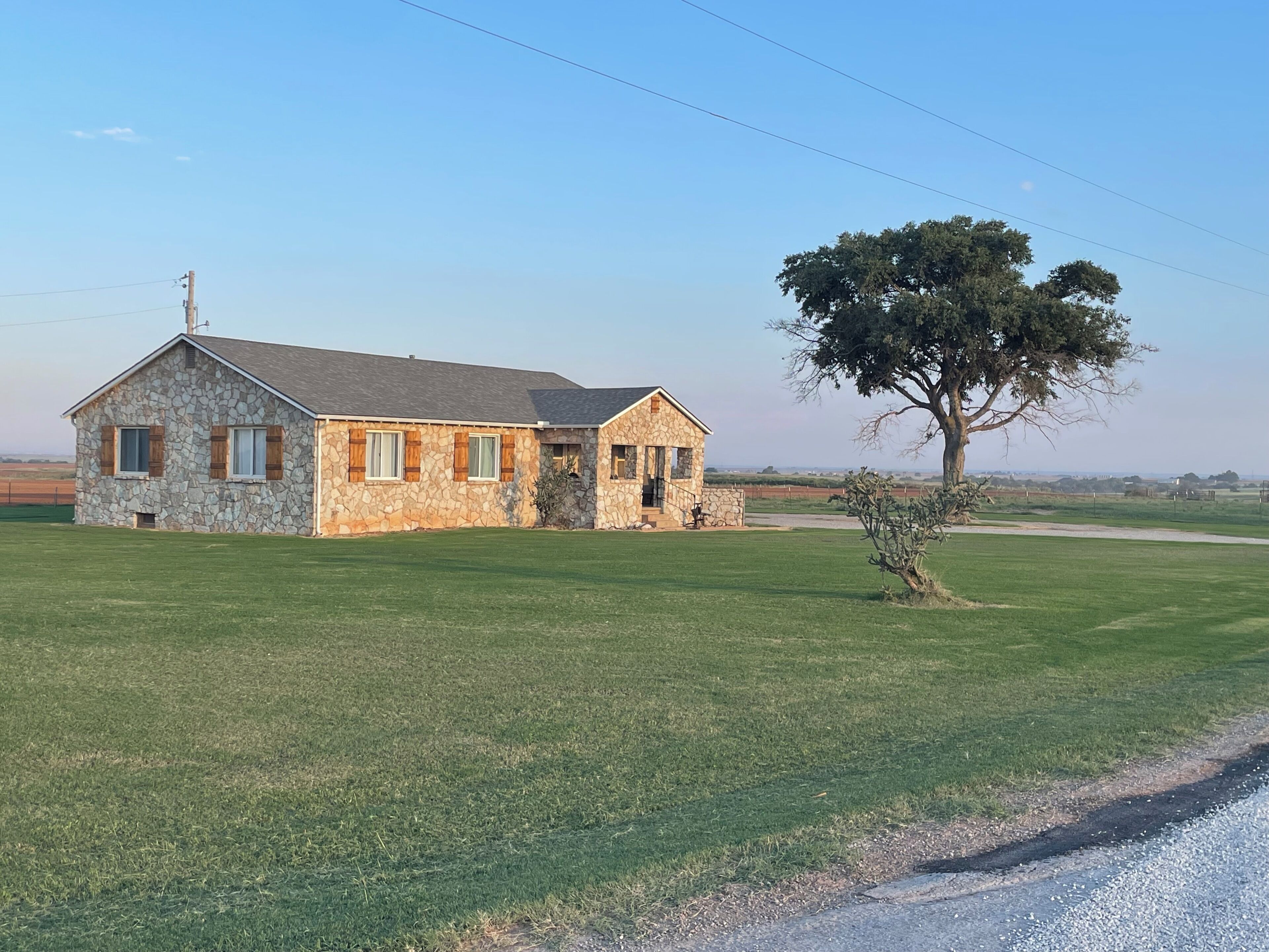 A stone house with a large lawn and a tree in front.