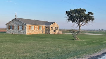 A stone house with a large lawn and a tree in front.