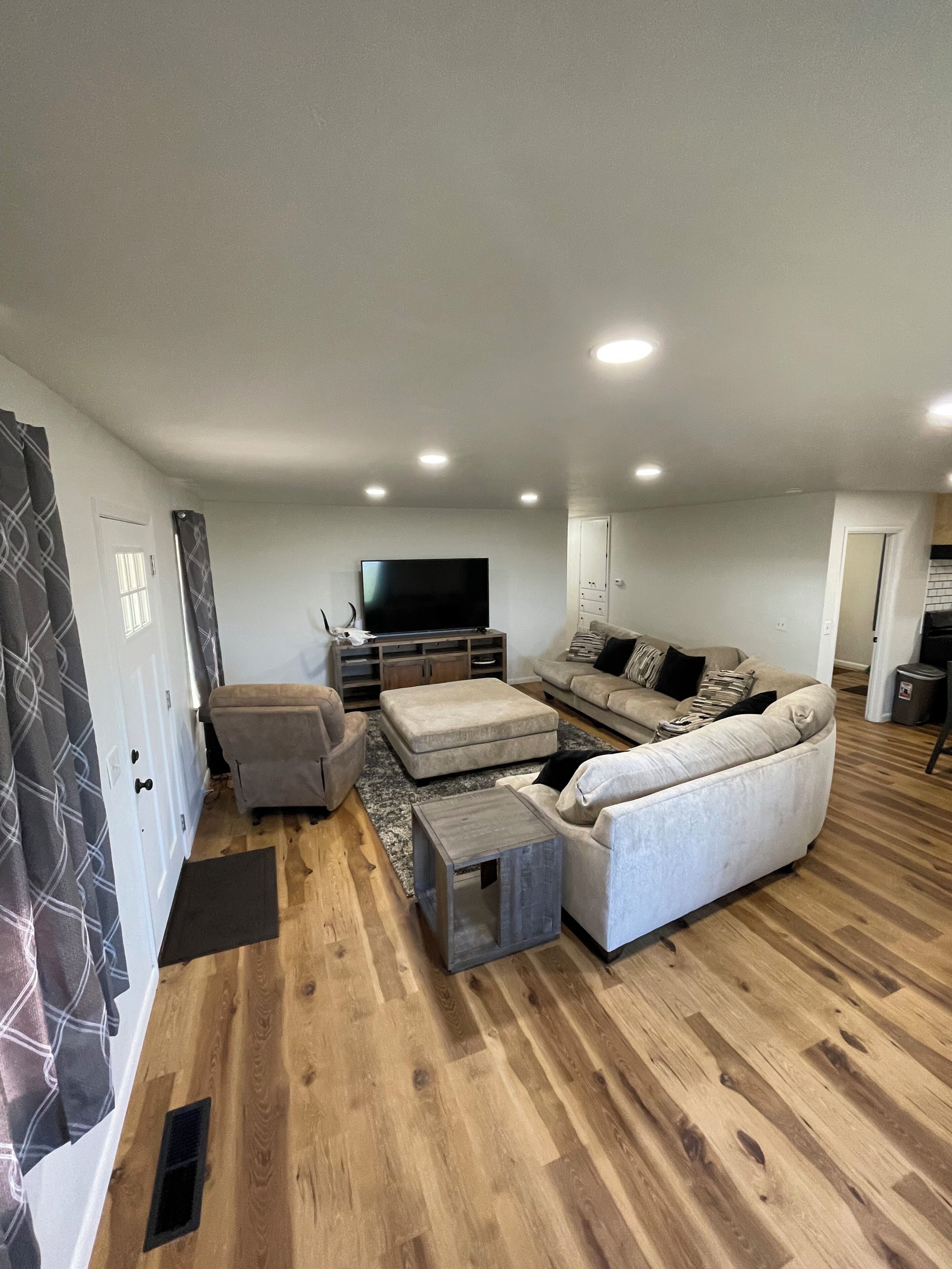 A modern living room with a sectional sofa, ottoman, and a flat-screen TV.