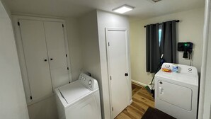 A laundry room with two washing machines, a dryer, and a ceiling vent.