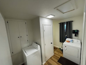 Un cuarto de lavandería con dos lavadoras, un secador y una rejilla de ventilación en el techo.