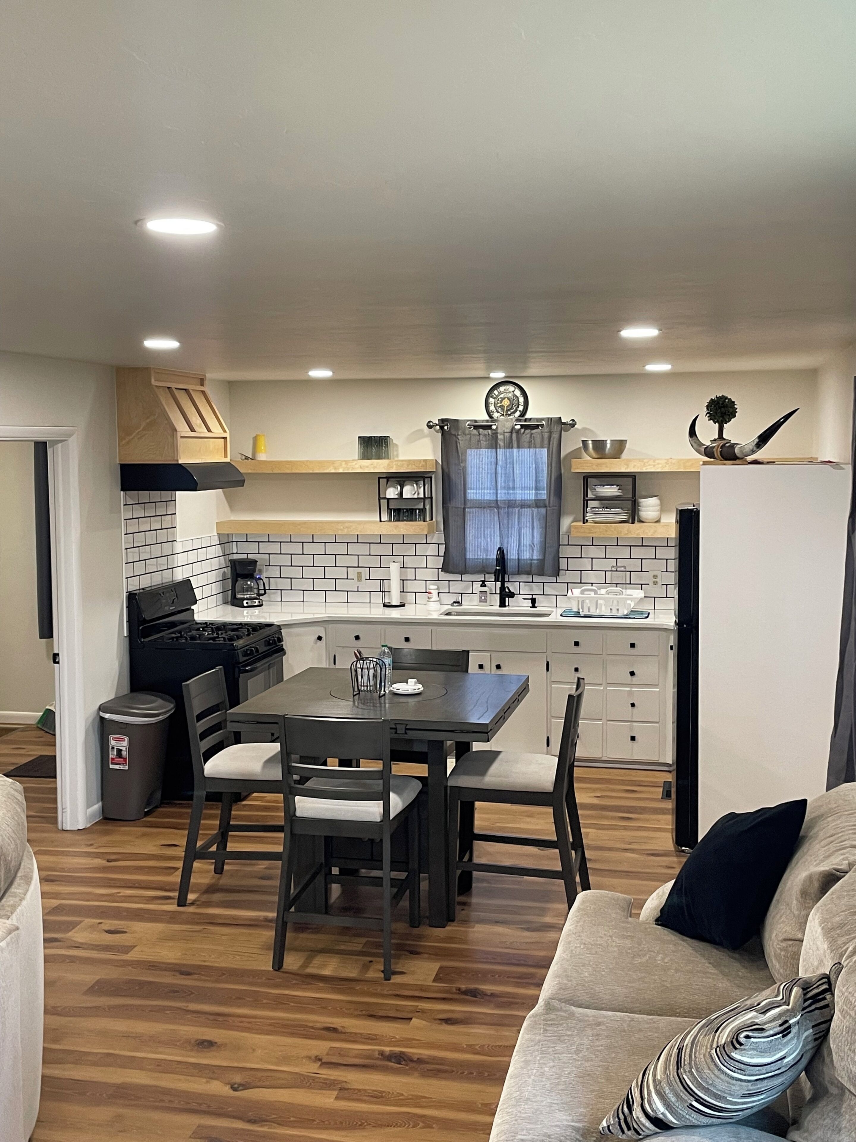 A modern kitchen with white cabinets, a dining table with chairs, and a refrigerator.
