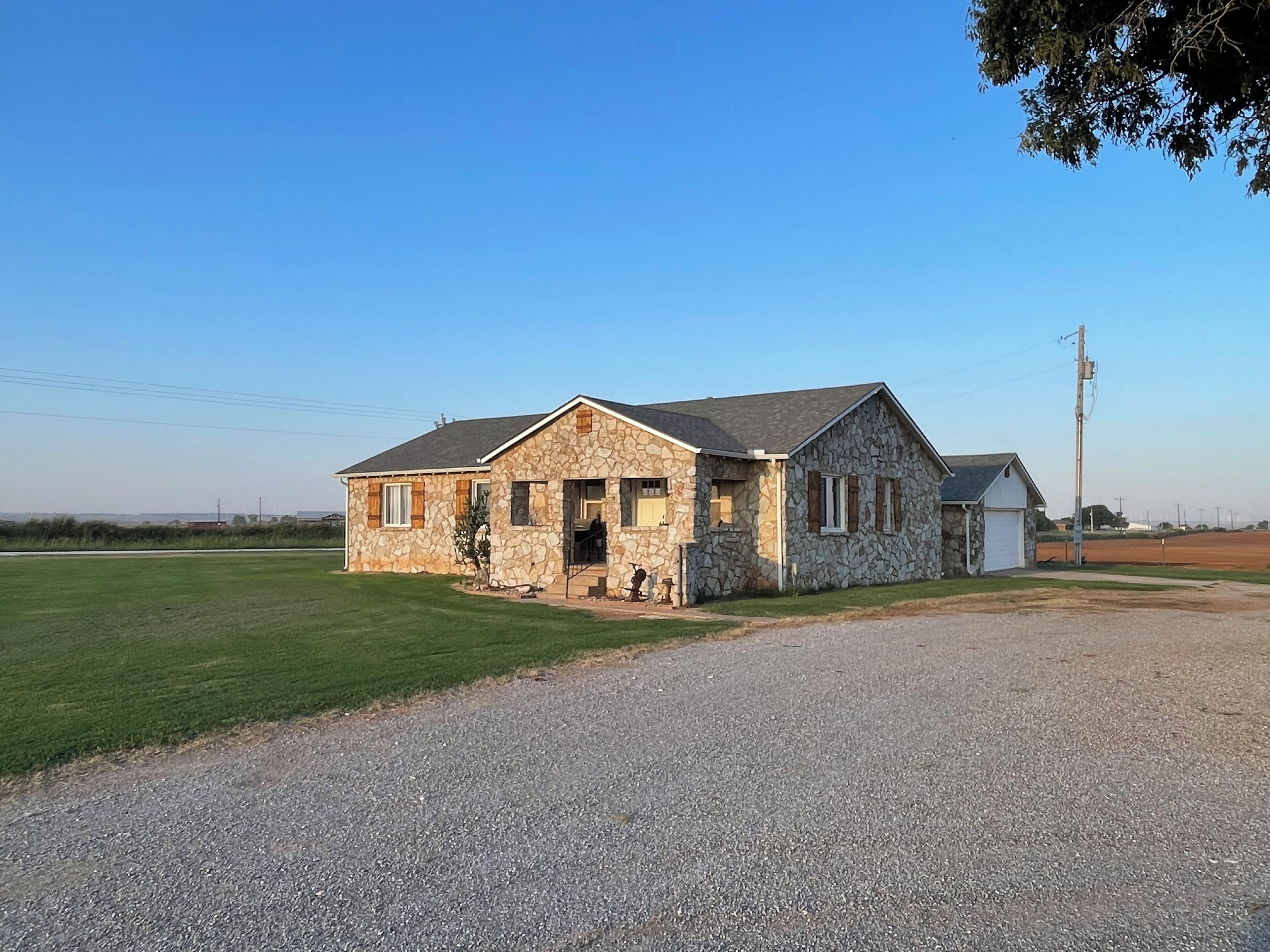 A stone building with a gravel driveway, a small attached garage, and a clear sky.