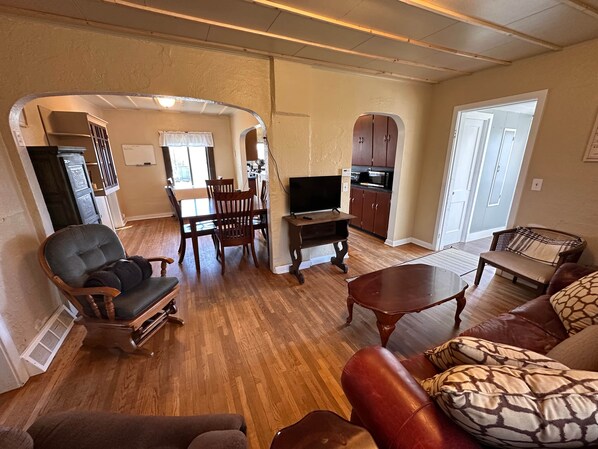 A living room with a dining area, kitchen, and a door leading to another room.