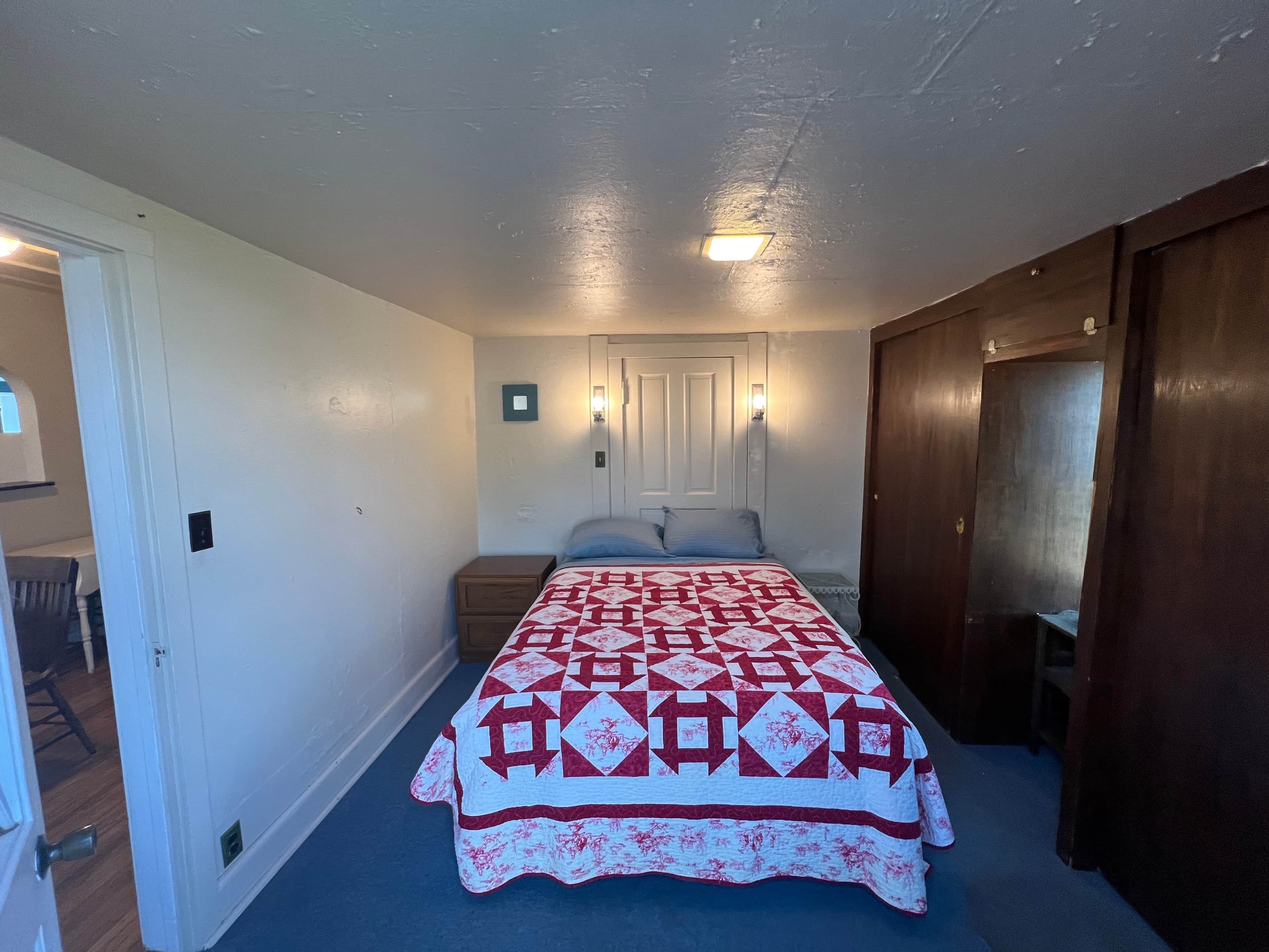 Ein Schlafzimmer mit Bett, Nachttisch, einer Tür und einer Wandleuchte.