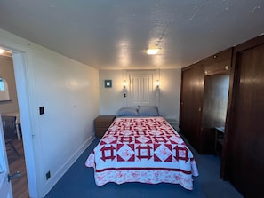 A bedroom with a bed, a nightstand, a door, and a wall-mounted light fixture.