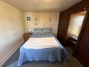 Un dormitorio con cama, mesitas de noche, una puerta y una pequeña mesa con lámpara.