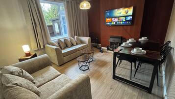 A living room with a sofa, armchairs, a coffee table, a fireplace, a television, and a dining table with chairs.