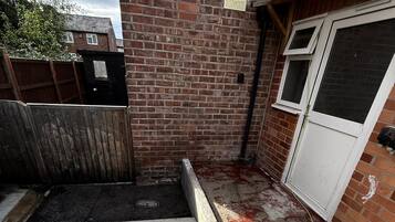 A brick wall with a window and a door, a concrete floor with a drain, and a wooden fence.