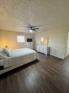 Ein Schlafzimmer mit Bett, Schminktisch, Spiegel, Deckenventilator und Holzboden.