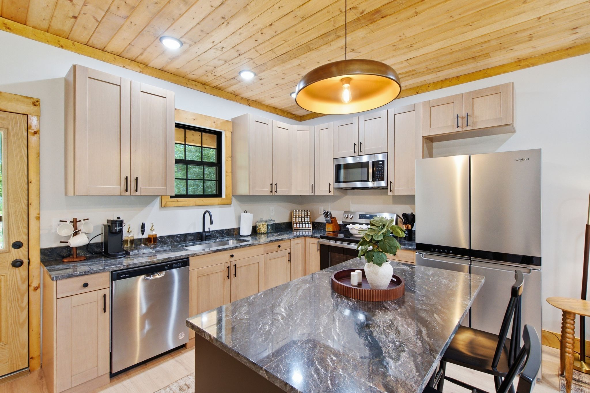 A modern kitchen with wooden cabinets, stainless steel appliances, a marble countertop, and a central island with a plant.
