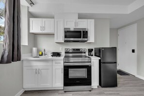 Une cuisine moderne avec des meubles blancs, un four à micro-ondes, un four et un réfrigérateur en acier inoxydable.