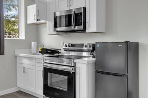 Una cocina moderna con electrodomésticos de acero inoxidable, incluyendo un microondas, horno y refrigerador, y muebles de cocina blancos.