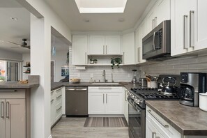 A modern kitchen with white cabinetry, a built-in microwave, a stove, and a coffee maker. - The Coastal Casa | Spa, Hoops & Garden Oasis (San Diego)