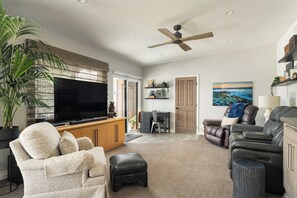 Ein Wohnzimmer mit Flachbildfernseher, Deckenventilator, Sofa, Massagesessel und einer großen Pflanze.