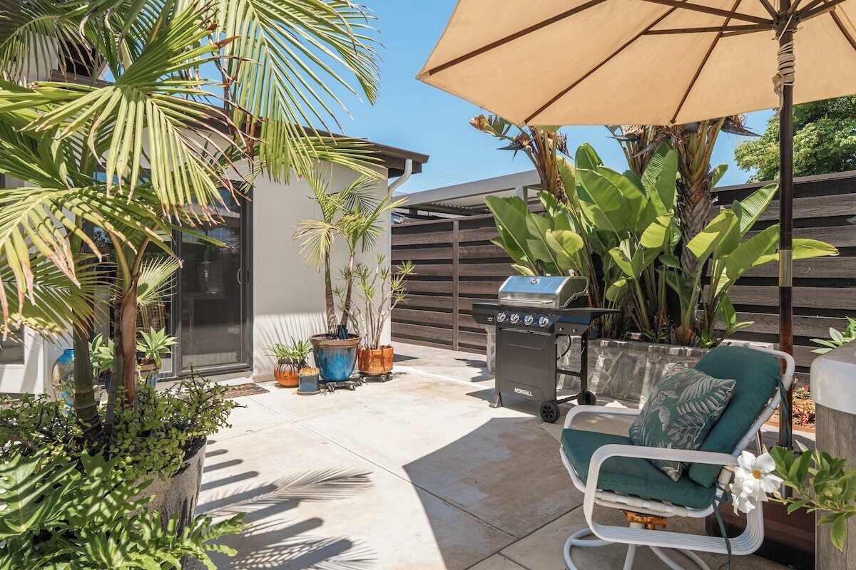 Une terrasse extérieure avec un barbecue, un fauteuil de relaxation et des plantes en pot.