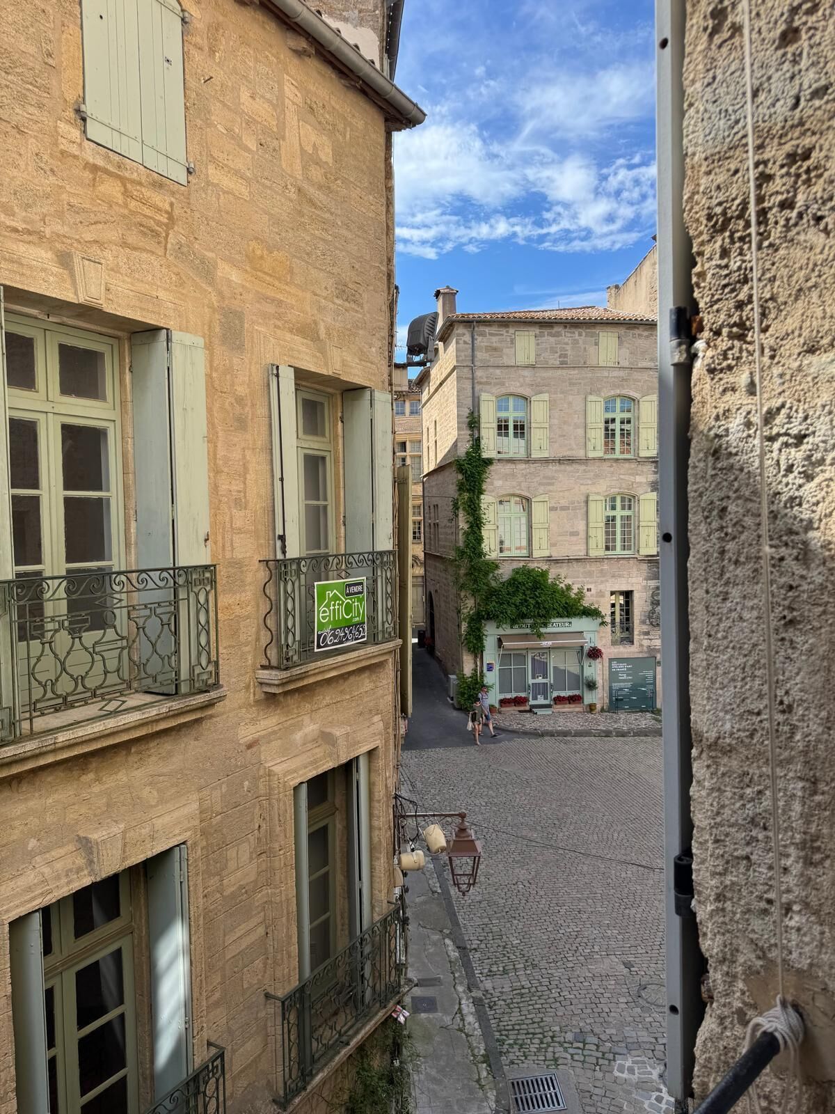 Une rue étroite, bordée de bâtiments de chaque côté, avec des balcons ornés de rampes en métal et un chemin pavé.