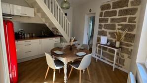 Uma sala de jantar com mesa e cadeiras de madeira, uma escada e uma parede de pedra.