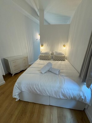 Een slaapkamer met een bed, bedlampen, een nachtkastje en een kaptafel.