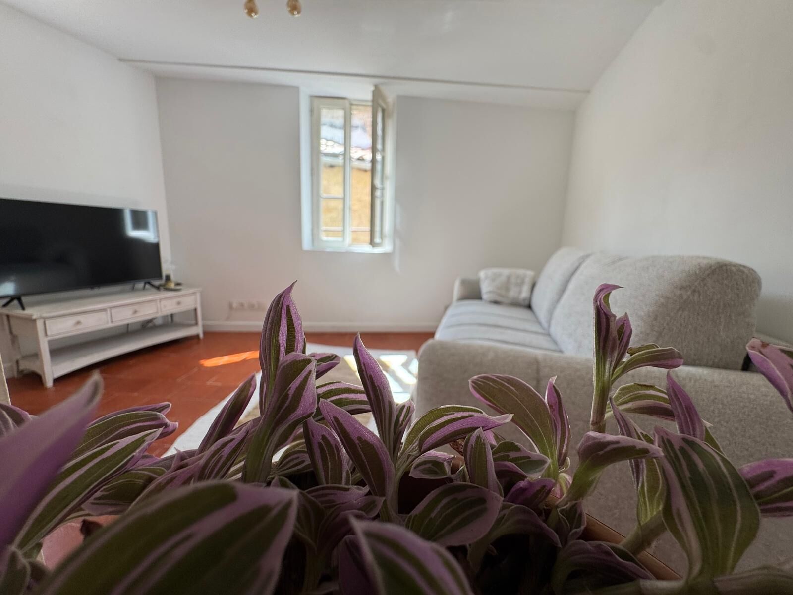 A living room with a sofa, a flat-screen TV on a stand, and a window with blinds.