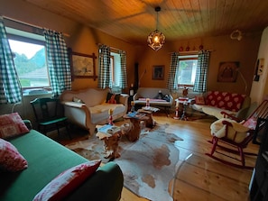 Ein gemütliches Wohnzimmer mit Holzbalkendecke, einem grünen Sofa, einem weißen Sofa, einem Schaukelstuhl und einem Couchtisch.
