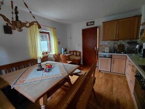 Ein Essbereich mit Holztisch und Stühlen, eine Küche mit Holzausstattung und ein Fenster mit Vorhängen.